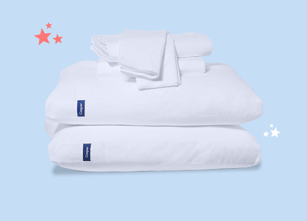 Folded pillowcases and sheet sets on top of two stacked pillows against a light blue background.