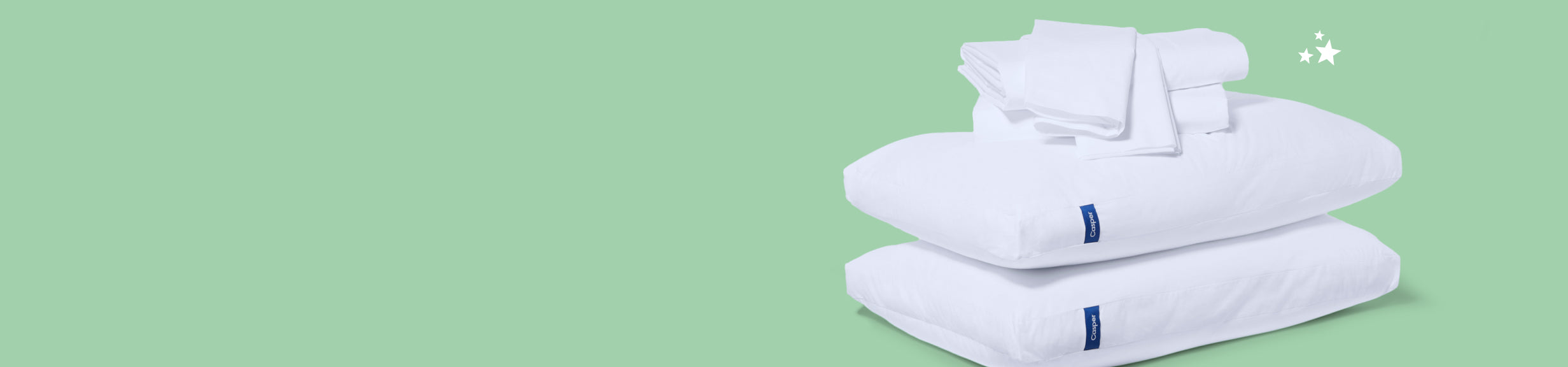 Two pillows stacked on top of each other with folded pillowcases and sheets on top of them