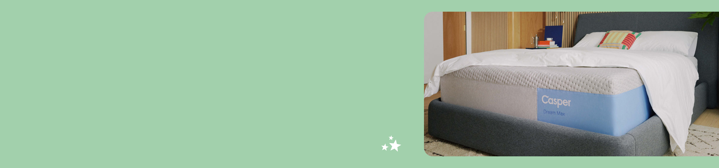 The Casper Dream Max mattress on a bed frame with a folded blanket and pillows on top. Corner view.