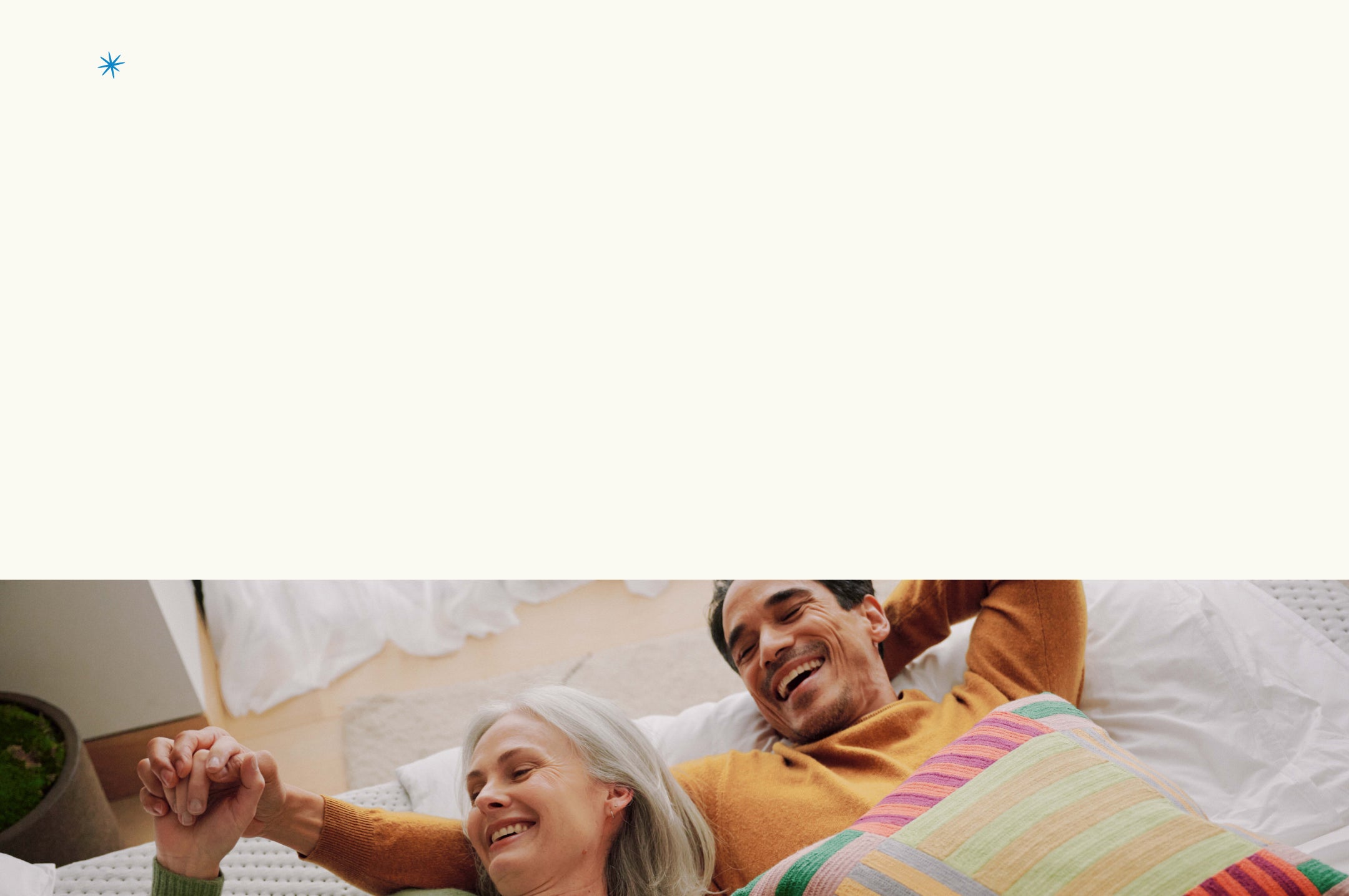 Man and woman lying on a bed holding hands, smiling.