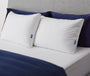 Casper's Original Pillow Double Pack leaning against two navy blue shams on a bed