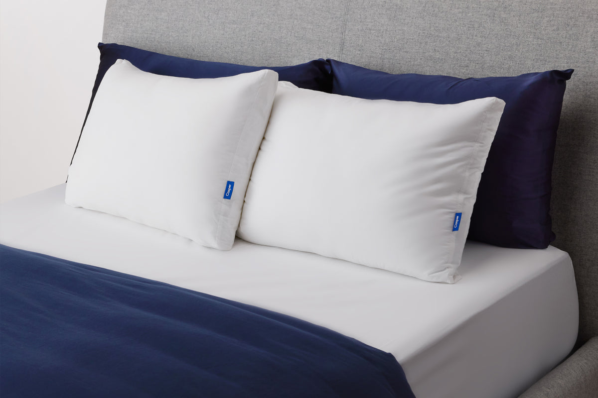 Casper's Original Pillow Double Pack leaning against two navy blue shams on a bed