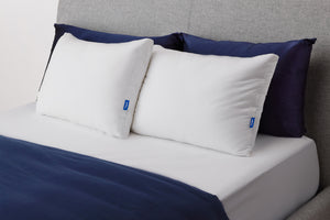 Casper's Original Pillow Double Pack leaning against two navy blue shams on a bed