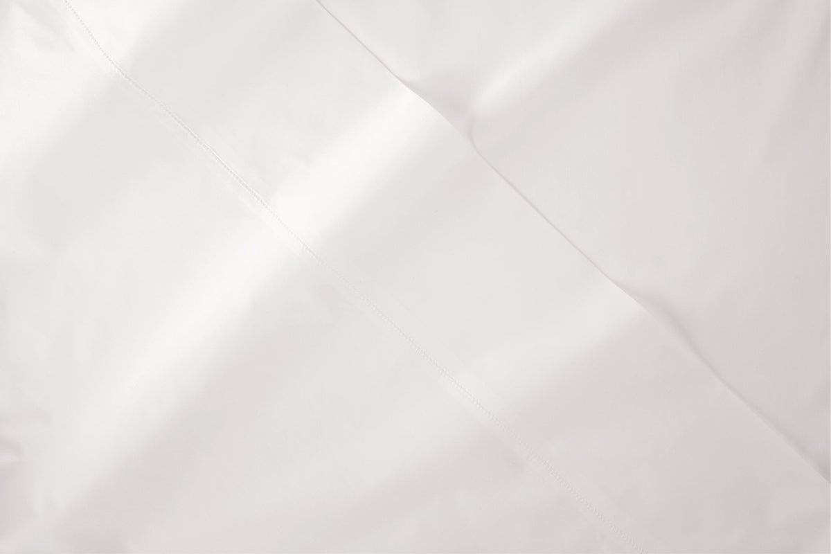 A close-up of a white bed sheet fabric with soft folds and a smooth texture