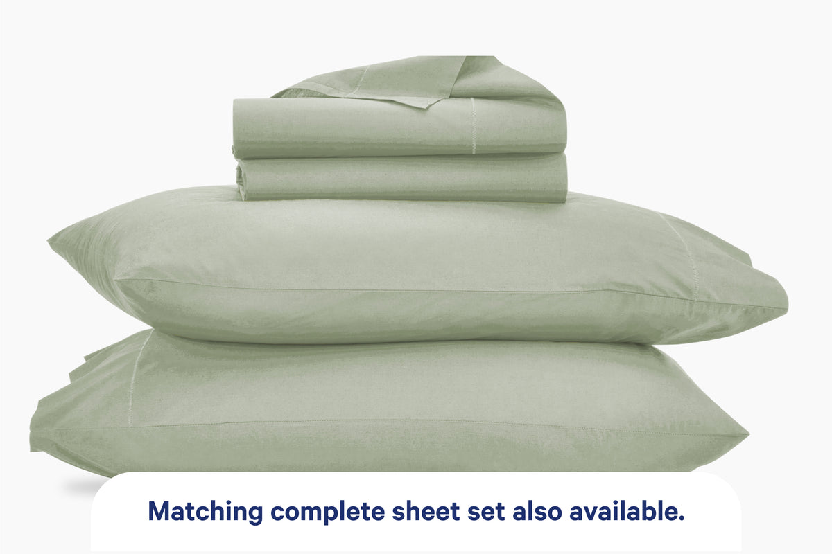 Two stacked eucalyptus-green pillows with folded eucalyptus-green bedding on top, shown on a light background with the text 'Matching complete sheet set also available.' at the bottom