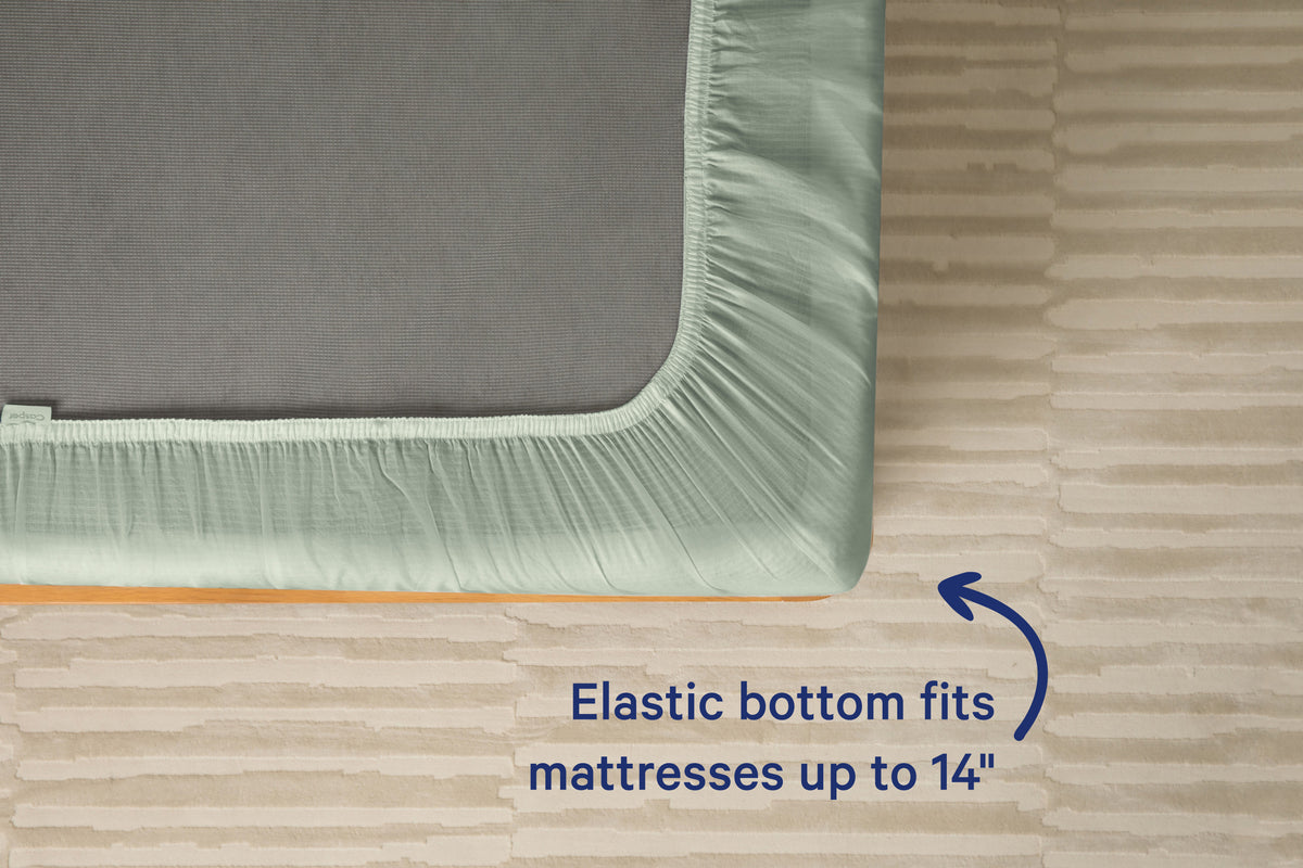 Underside view of a mattress with a eucalyptus-green fitted sheet. Text on the image reads 'Elastic bottom fits mattresses up to 14 inches.'