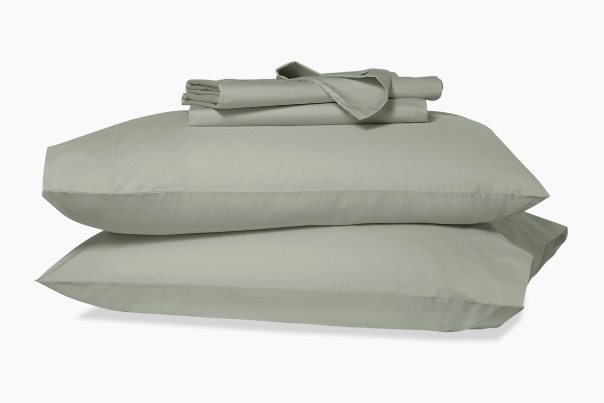 Folded sheets on top of two stacked pillows in pillowcases. Eucalyptus-green colorway.