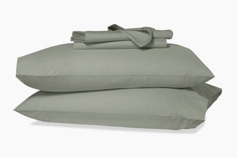 Folded sheets on top of two stacked pillows in pillowcases. Eucalyptus-green colorway.