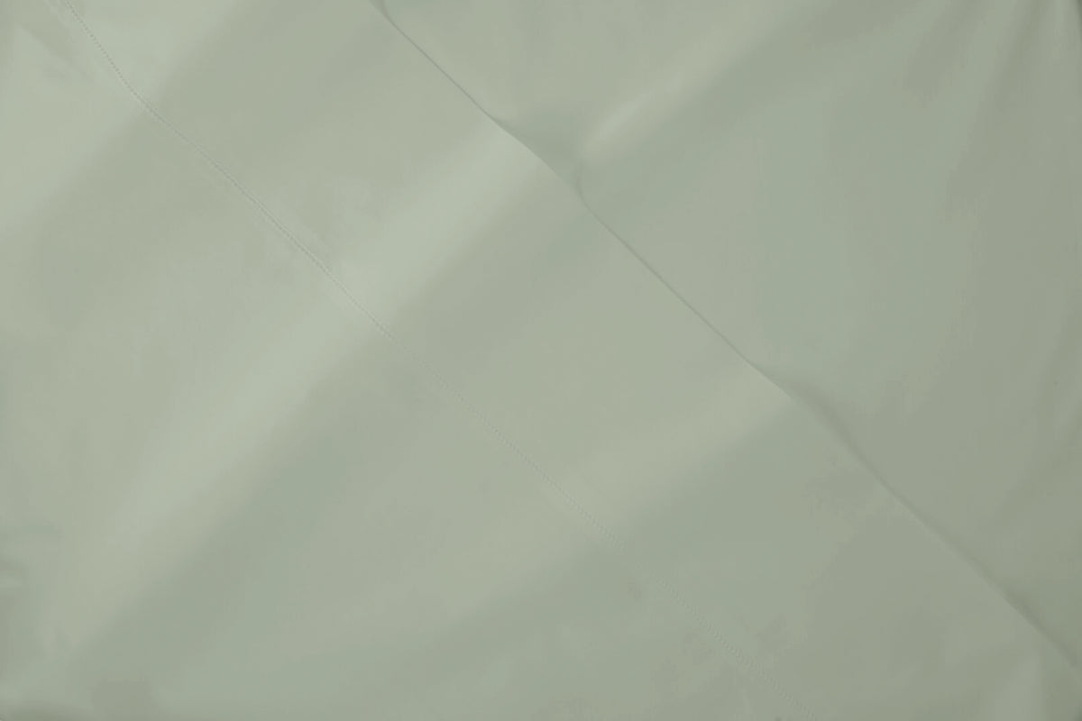 A close-up of a Eucalyptus green bed sheet fabric with soft folds and a smooth texture