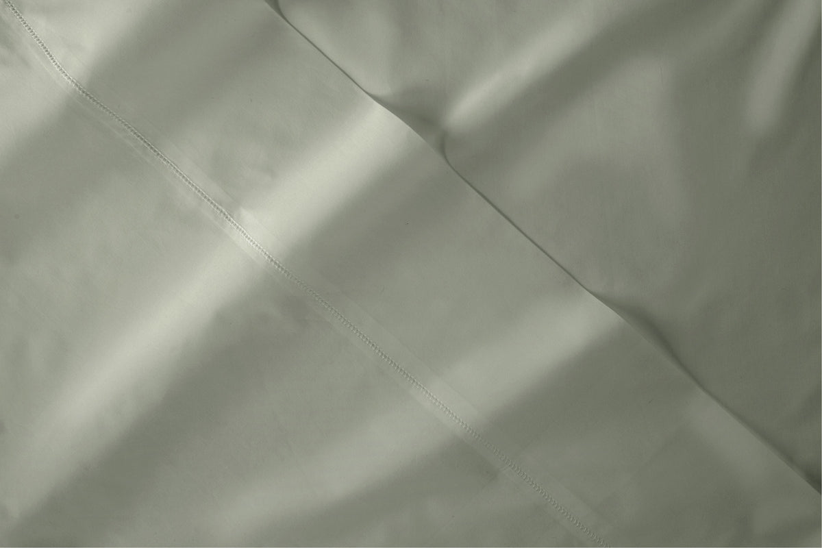A close-up of a eucalyptus-green bed sheet fabric with soft folds and a smooth texture