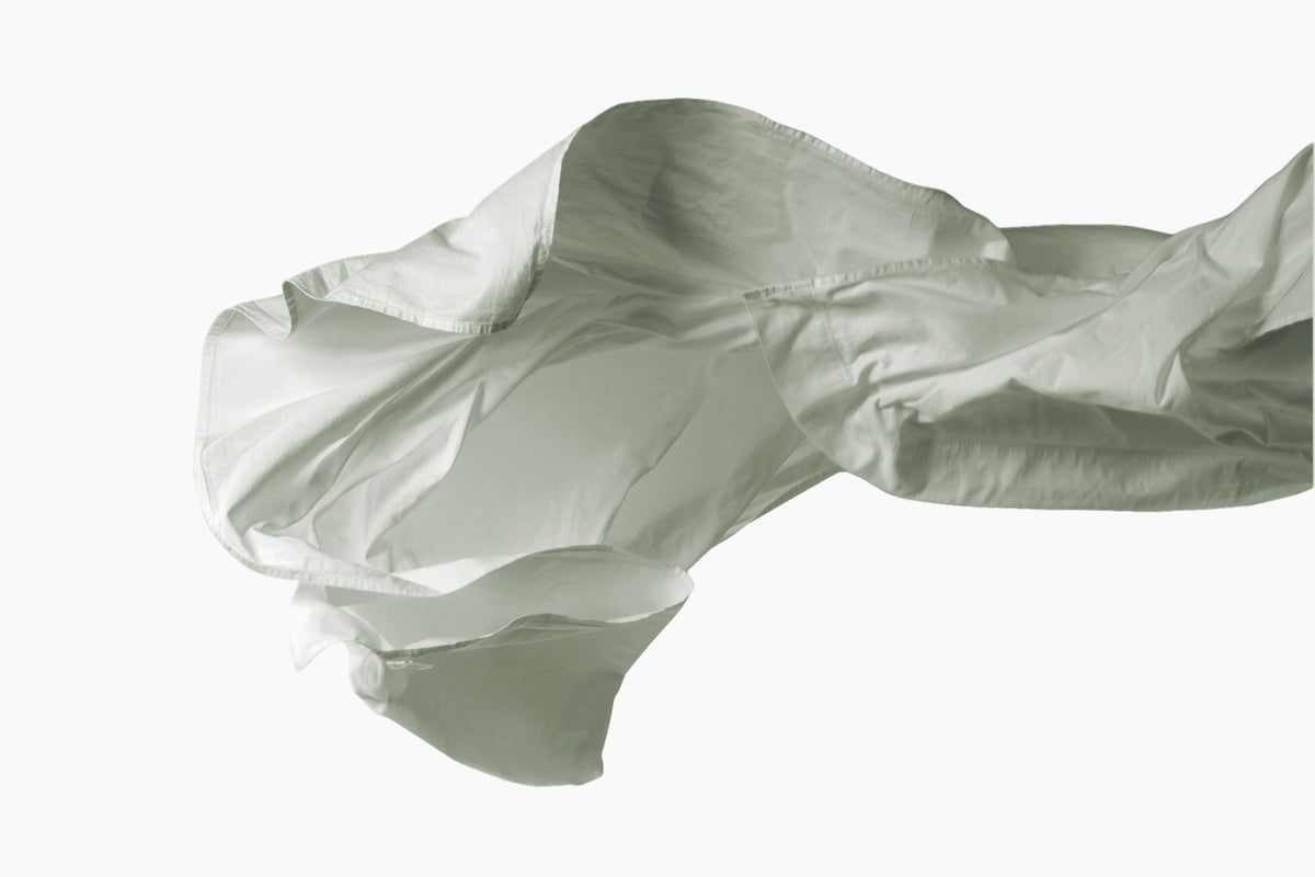 A still shot of a eucalyptus-green bed sheet being tossed in the air against a white background