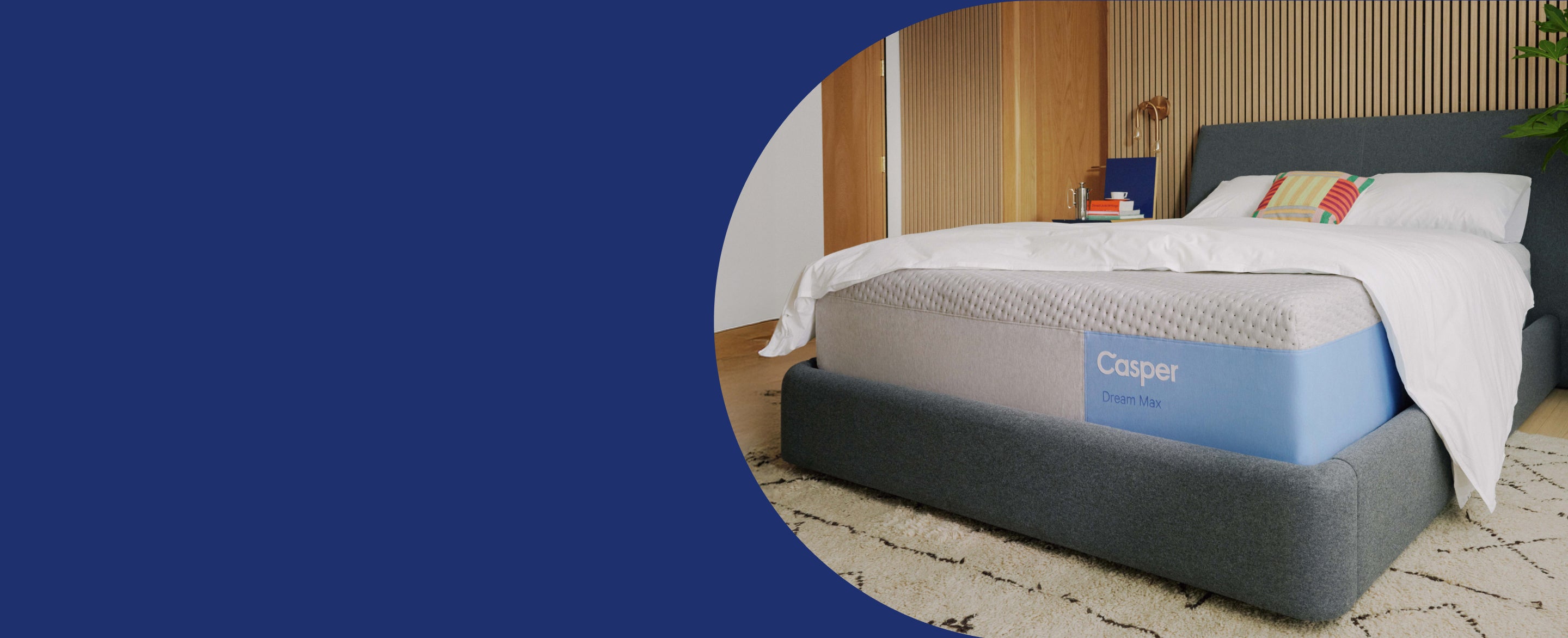 Casper's Dream Max on a fabric bed frame with a headboard. A blanket and pillows sit atop the bed in a bedroom setting.