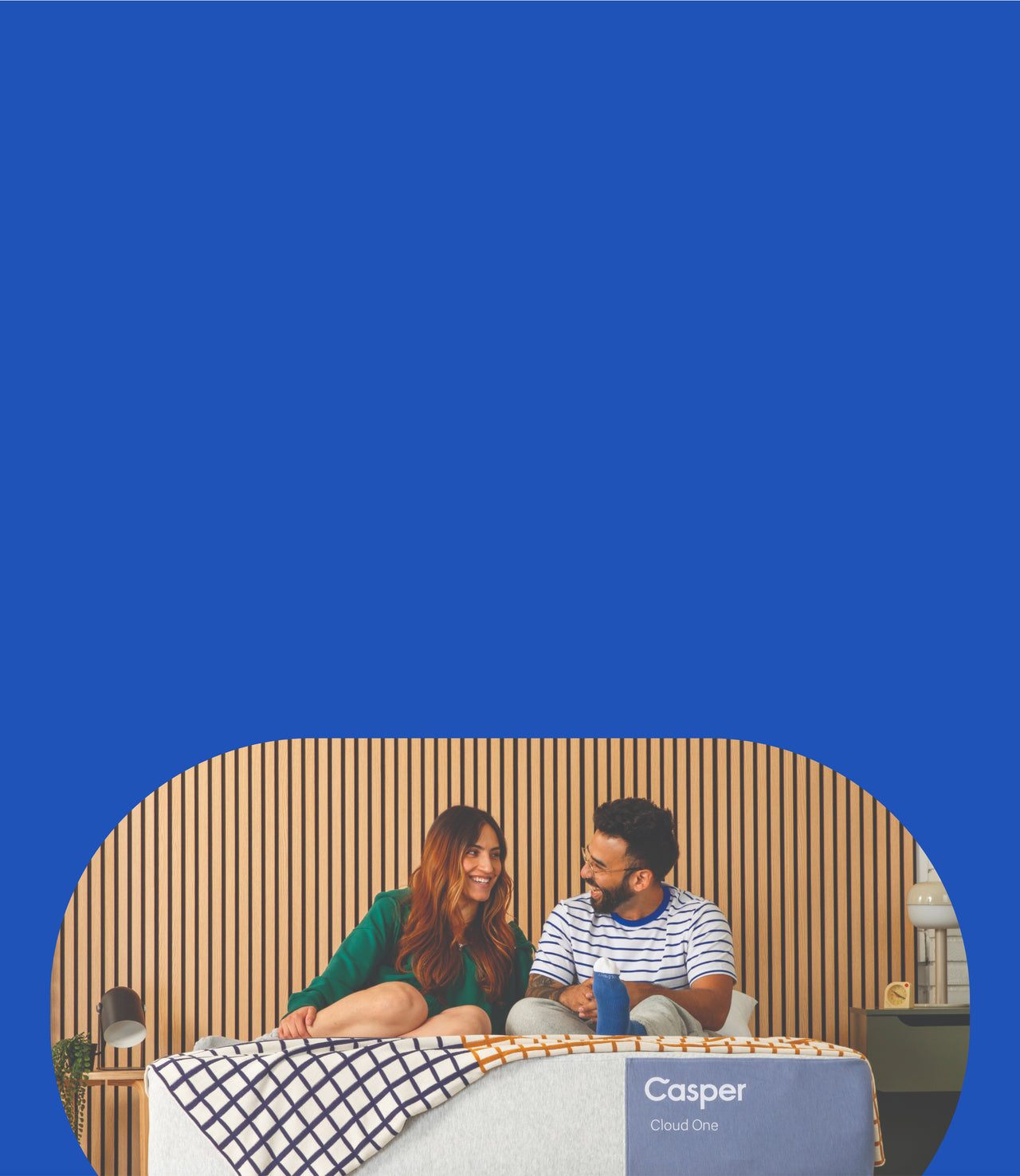 A couple sits and smiles on their Casper Cloud One mattress