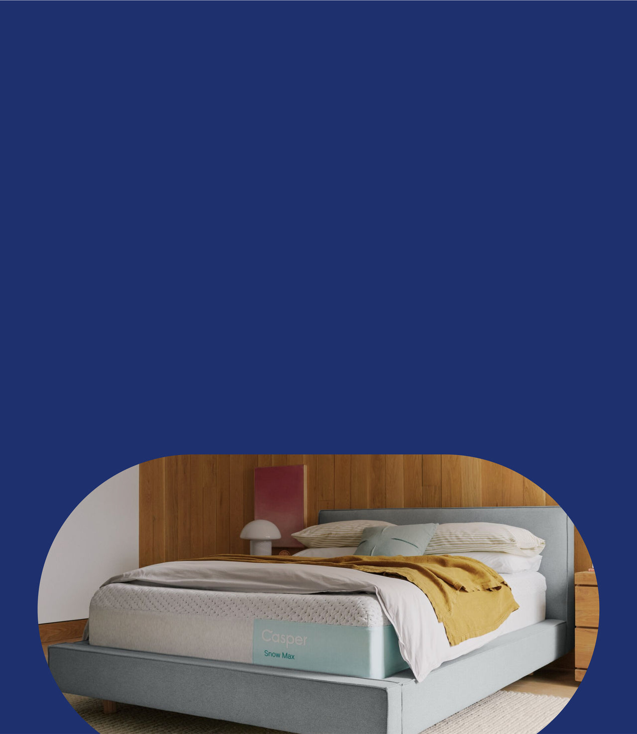Casper's Snow Max mattress on a bed frame with a blanket and pillows on top. 