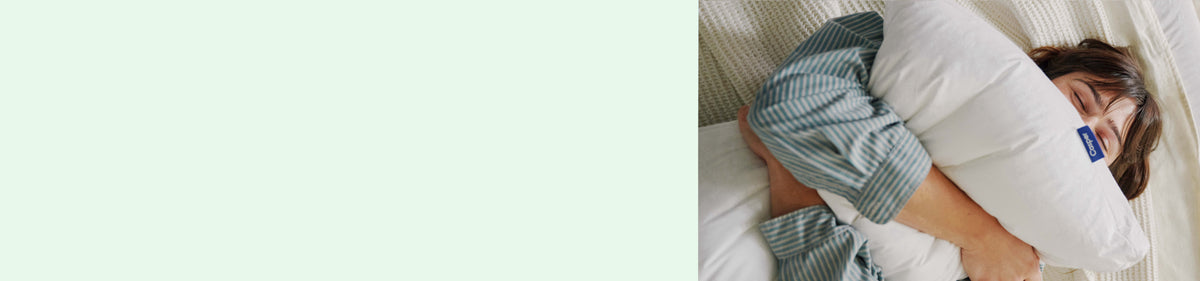 Light green background. Image of a woman squeezing a pillow in bed.