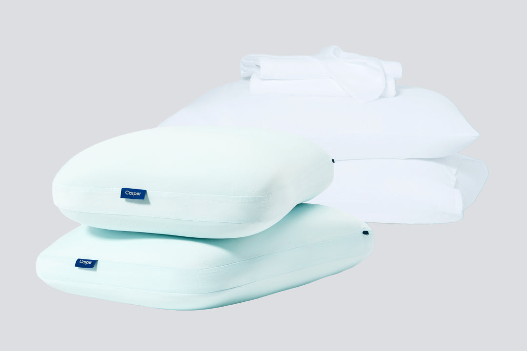 two hybrid snow pillows front with another two in the back. The back two are in pillowcases with a sheet set placed on top of them.