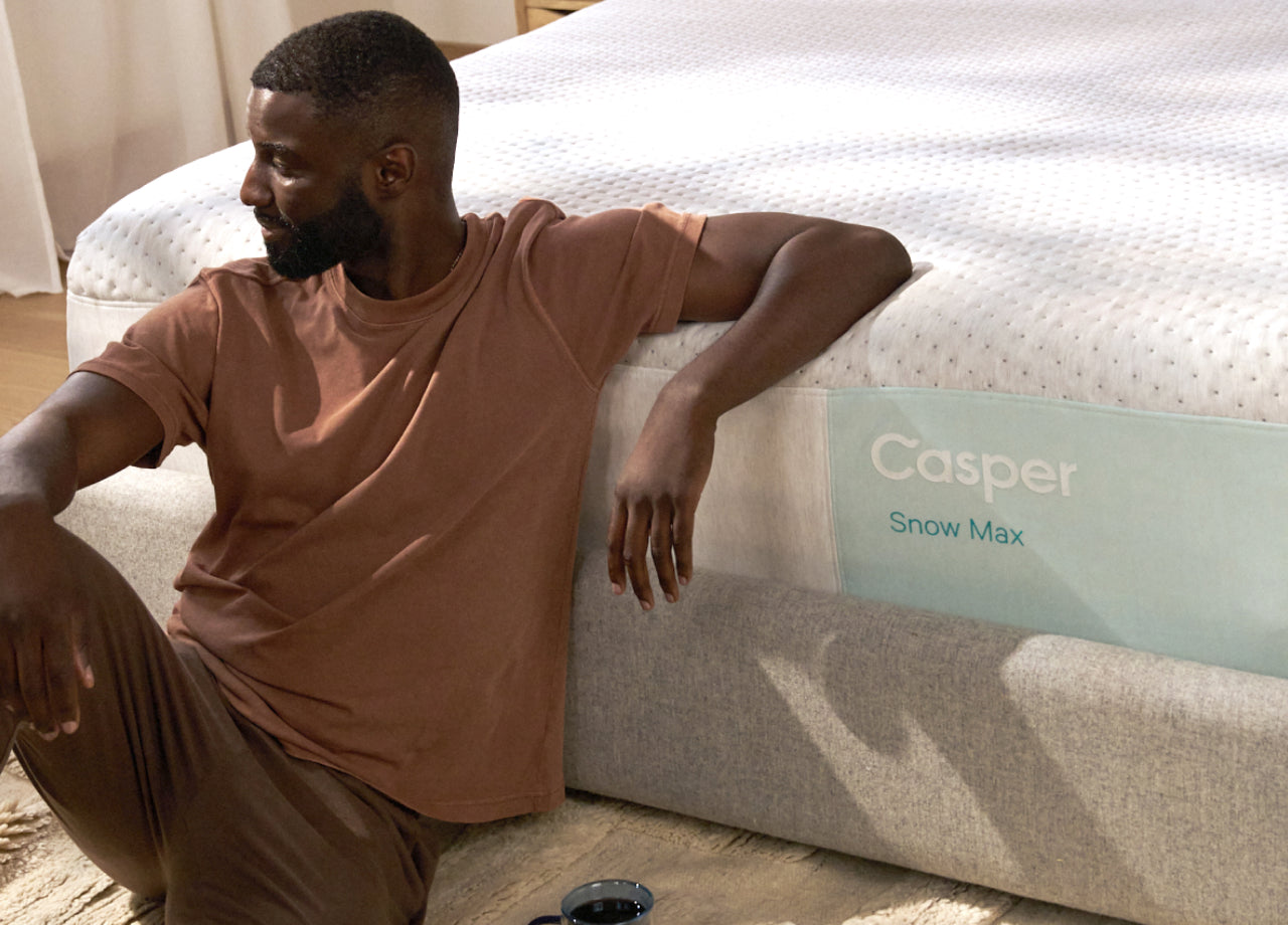 Front view of Casper's Snow Max mattress. A man sits on the floor, leaning back with his elbow on top of the mattress.