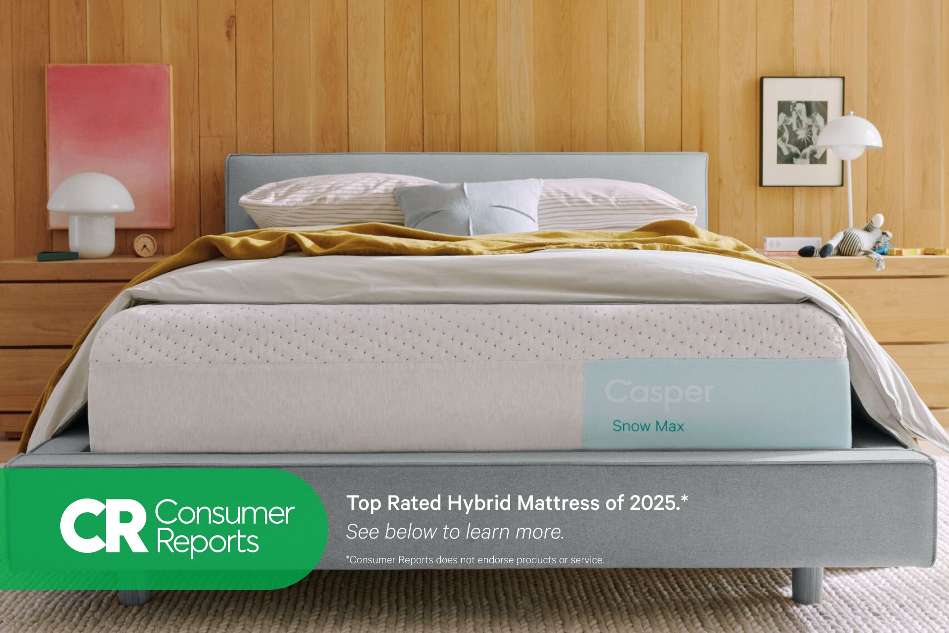 Front view of Casper's Snow Max mattress on a bed frame with pillows and a folded blanket on top. At the bottom of the image appears text that reads "Consumer Reports. Top rated hybrid mattress of 2025.* See below to learn more. *Consumer Reports does not endorse products or service."