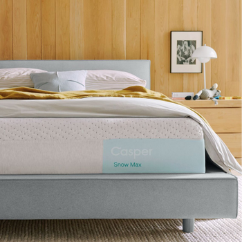 Casper's Snow Max mattress on a bed frame with pillows and a blanket folded on top.