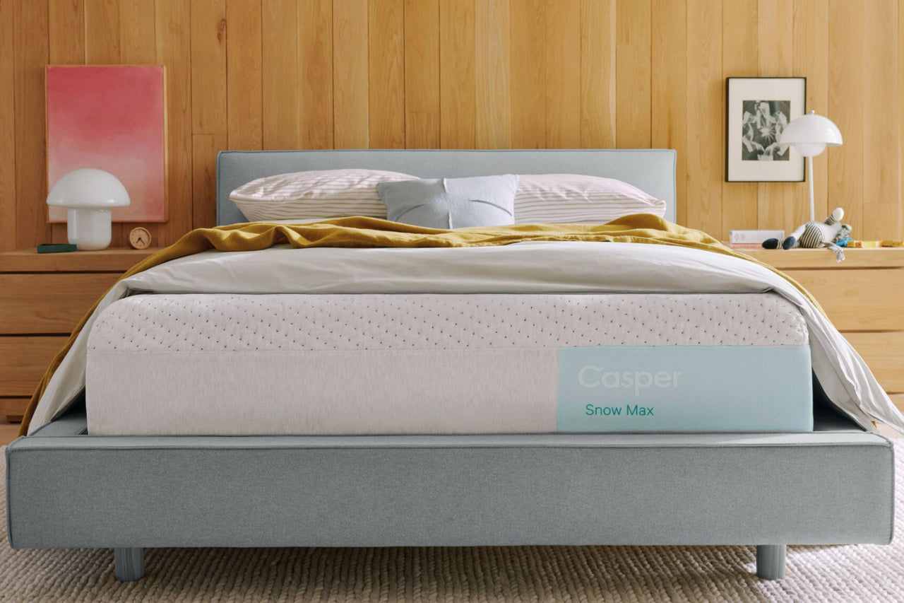 Casper's Snow Max mattress on a bed frame with pillows and a blanket folded on top.