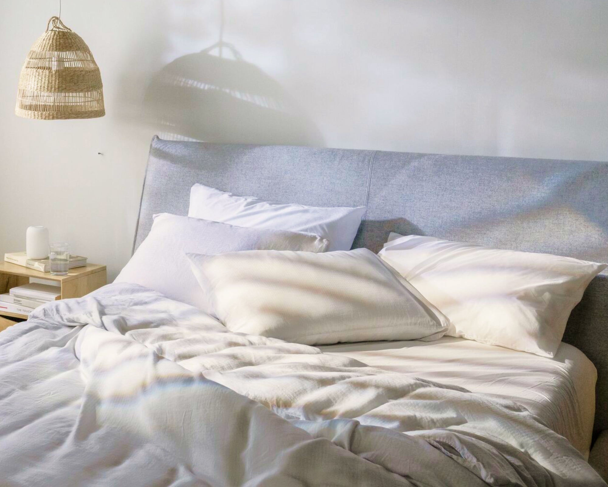 A fully made bed. The mattress is covered with a sheet, duvet, blanket folded on top, and there are four mattresses leaning back against a headboard.