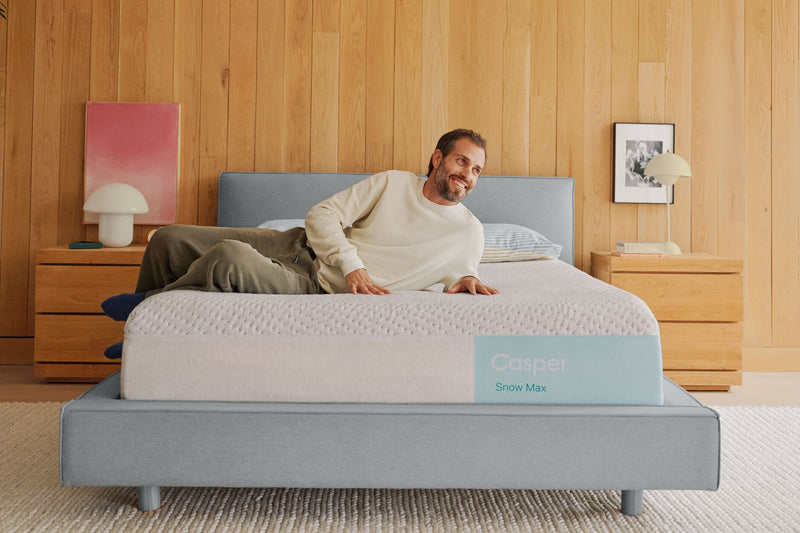 A man lies on his side smiling on a Casper Snow Max mattress.