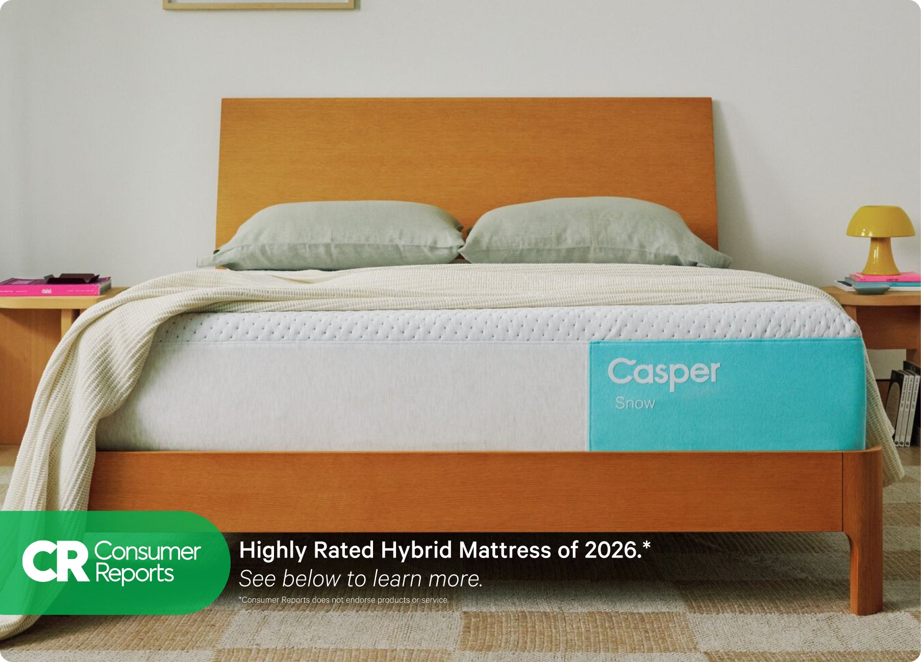 Front-view of the Casper Snow mattress in a bed frame with two pillows and a blanket folded on top. Beneath the image appears text which reads "Consumer Reports. Highly rated hybrid mattress of 2026.* See below to learn more. Consumer Reports does not endorse products or service."