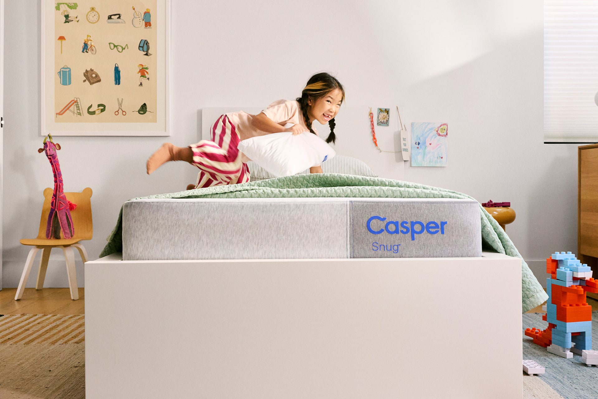Child playing on a Casper Snug mattress in a bedroom with toys and furniture.
