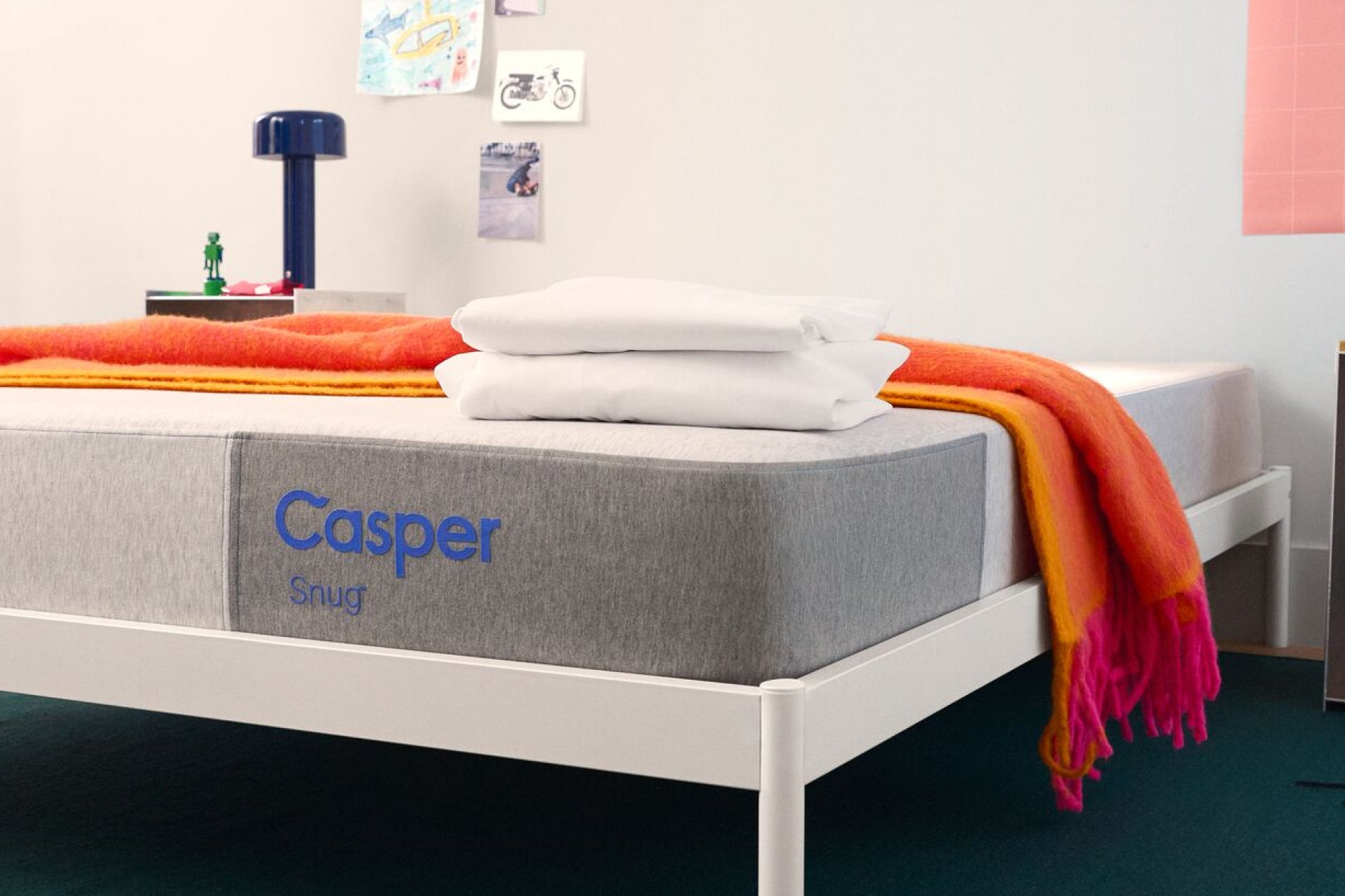Front-corner view of the Casper Snug mattress on a bed with colorful blankets and pillows in a bedroom setting.