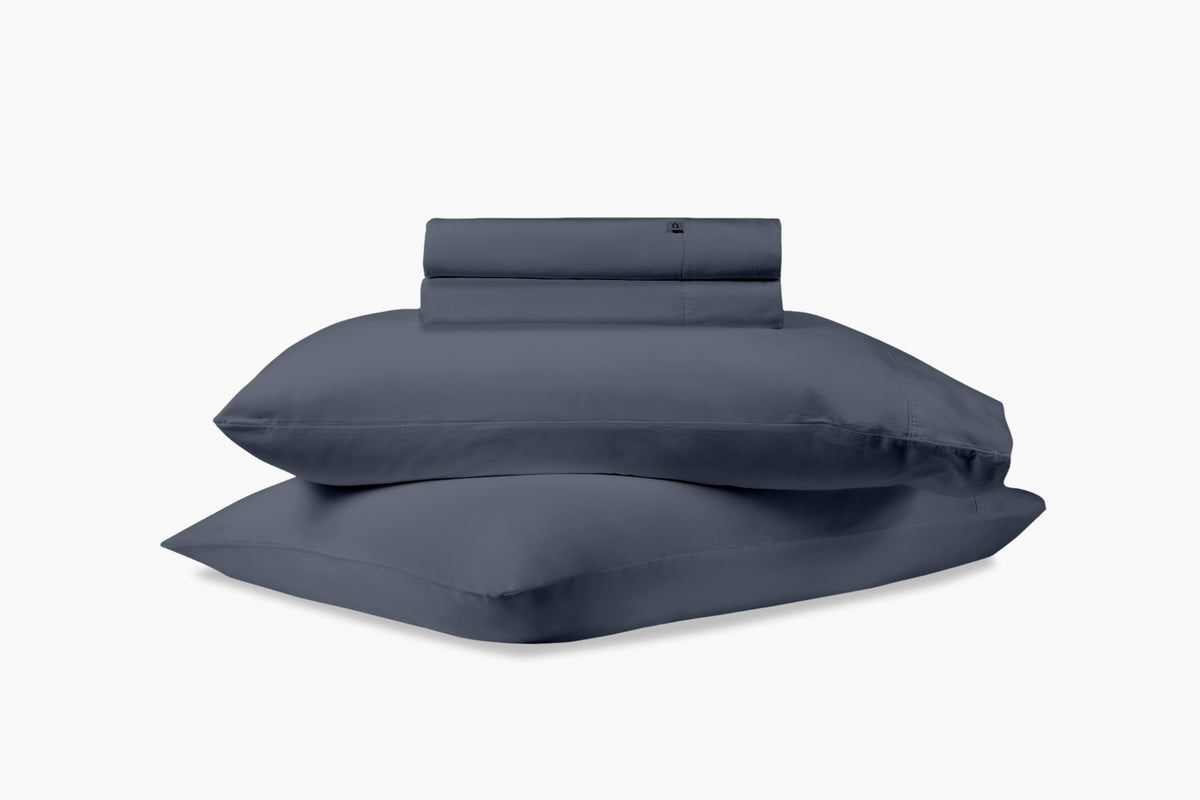 A stack of pillows and bed sheets, indigo colorway, against a white background