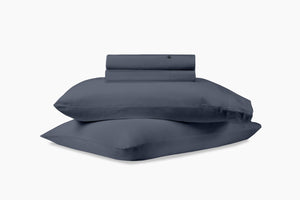 A stack of pillows and bed sheets, indigo colorway, against a white background