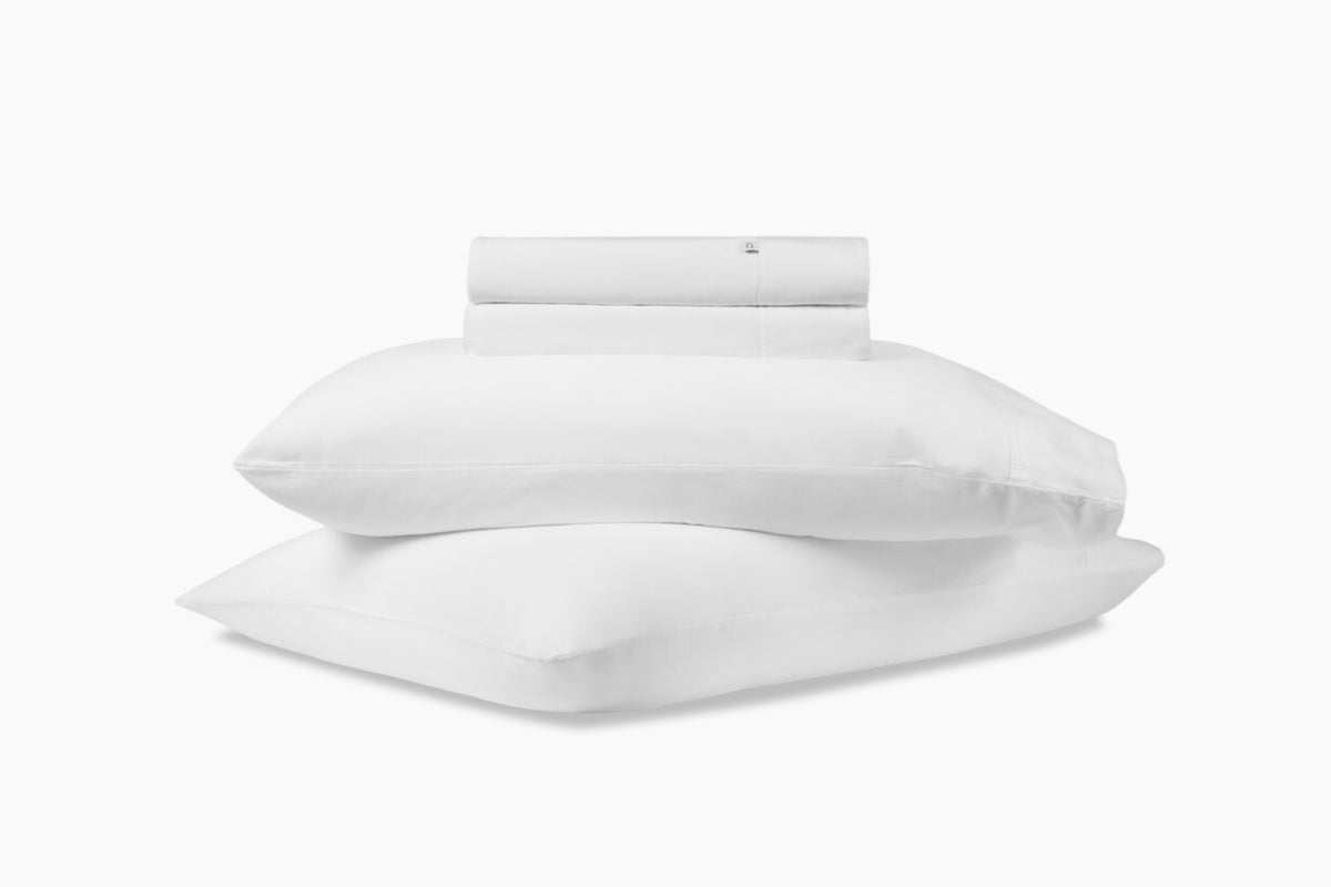 A stack of pillows and bed sheets, white colorway, against a white background