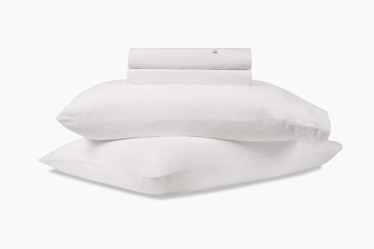 A stack of pillows and bed sheets, white colorway, against a white background
