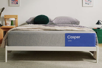 The One mattress on a bed frame with a blanket and pillows on top of it in a bedroom setting