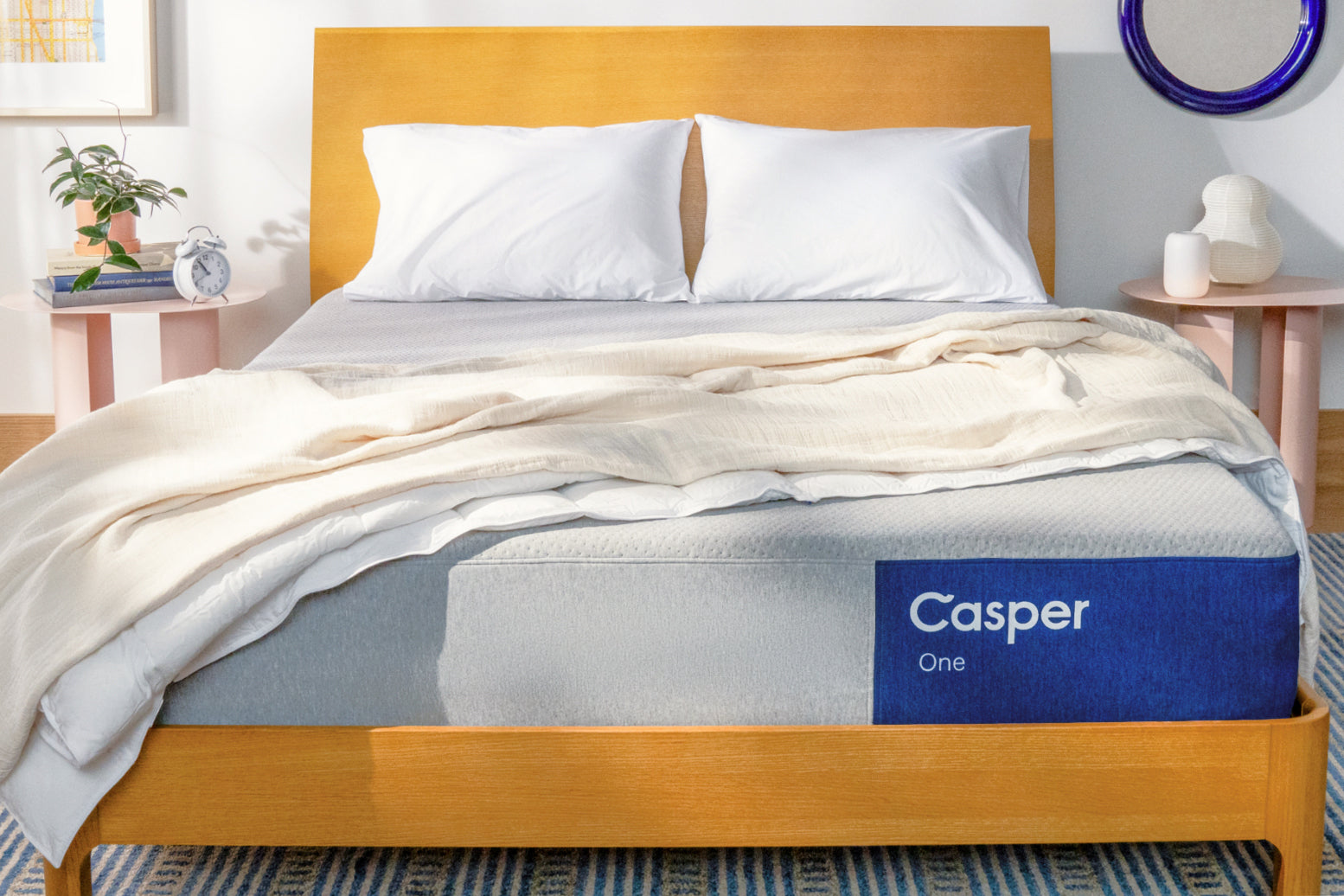 Front view image of the Casper One mattress on a bed. On top of the mattress is a folded blanket and two pillows leaning on the headboard.