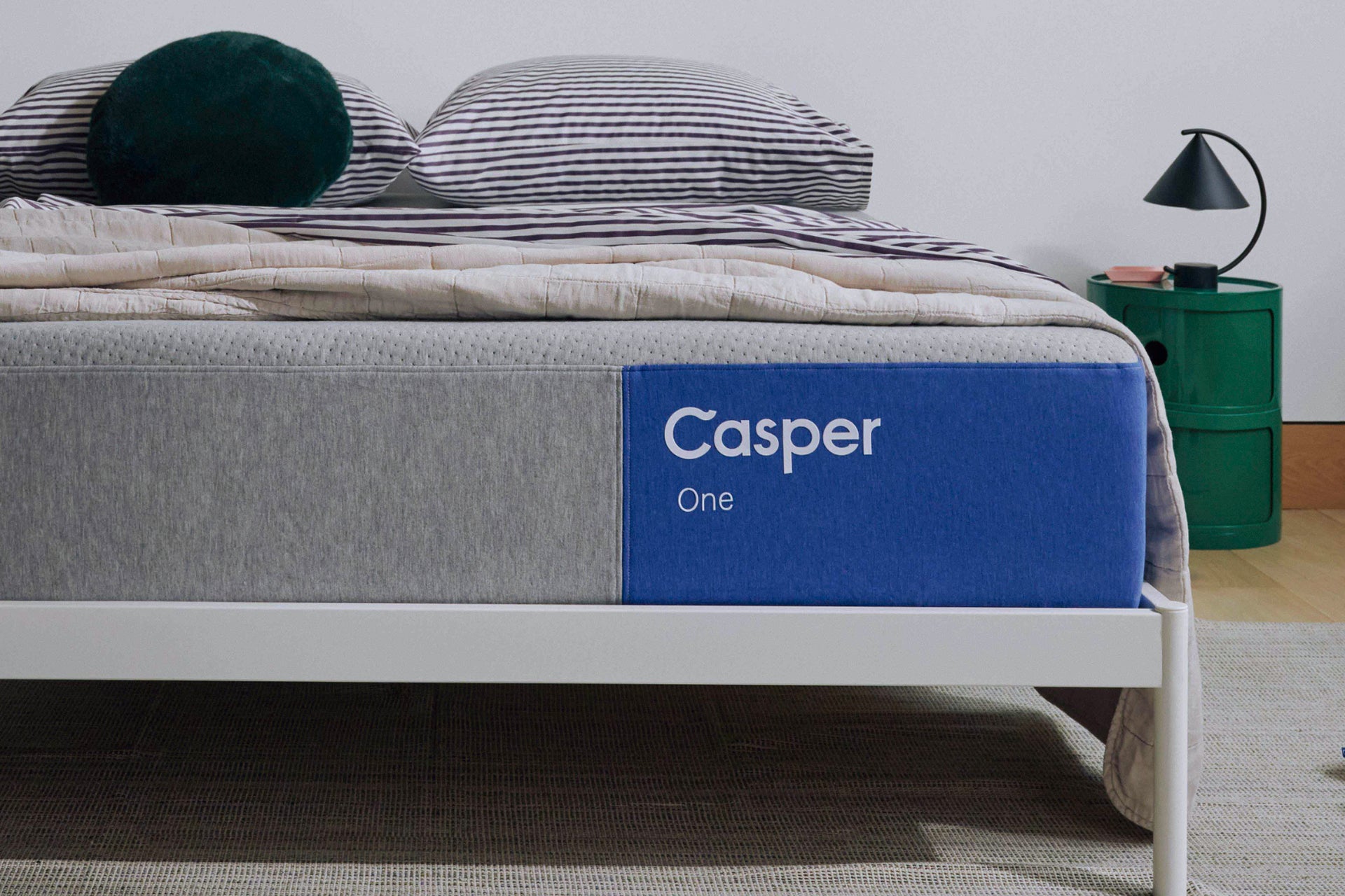 Casper's The One mattress on a bed with pillows and a lamp in the background