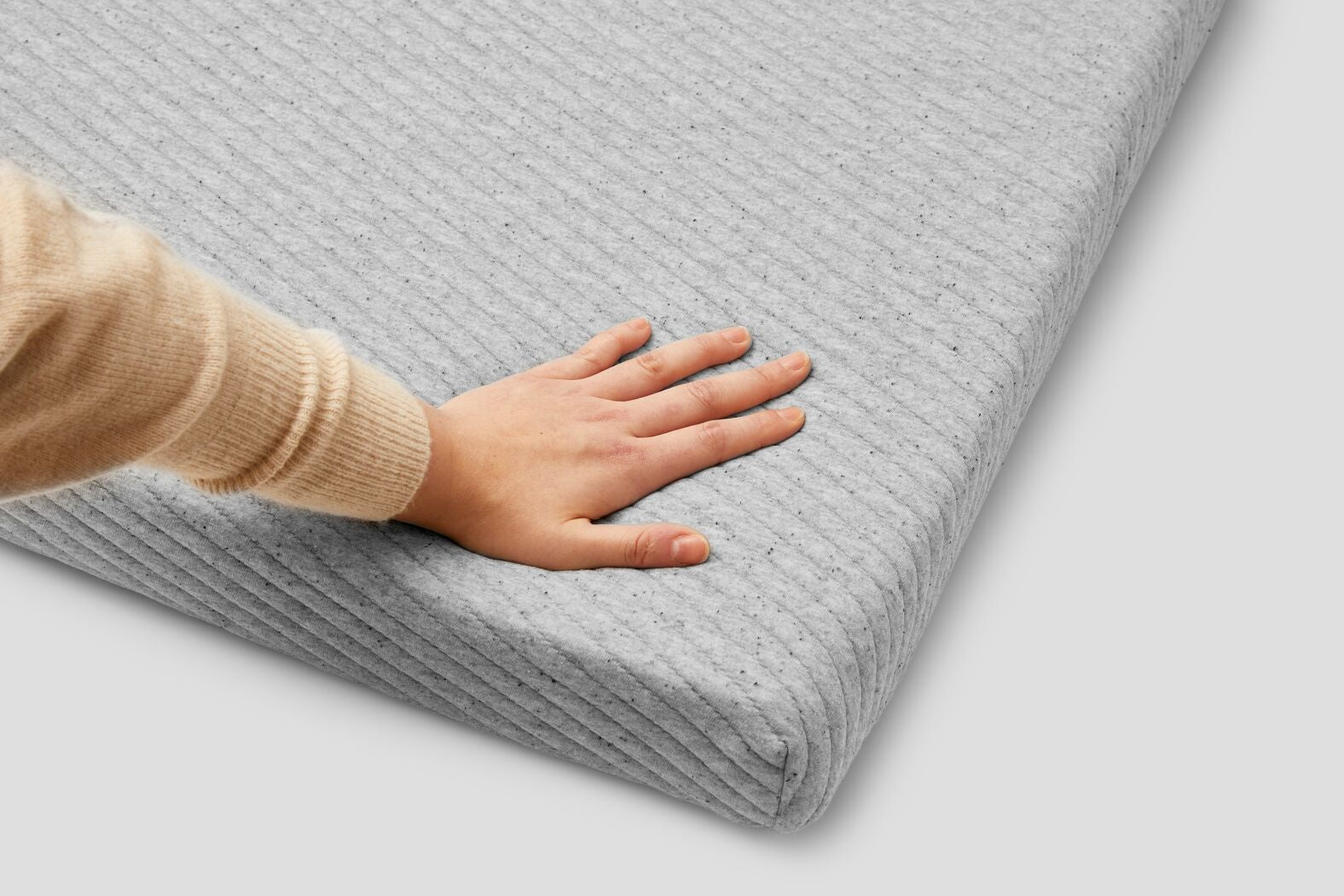 Close-up of someone's hand touching the corner of a mattress topper