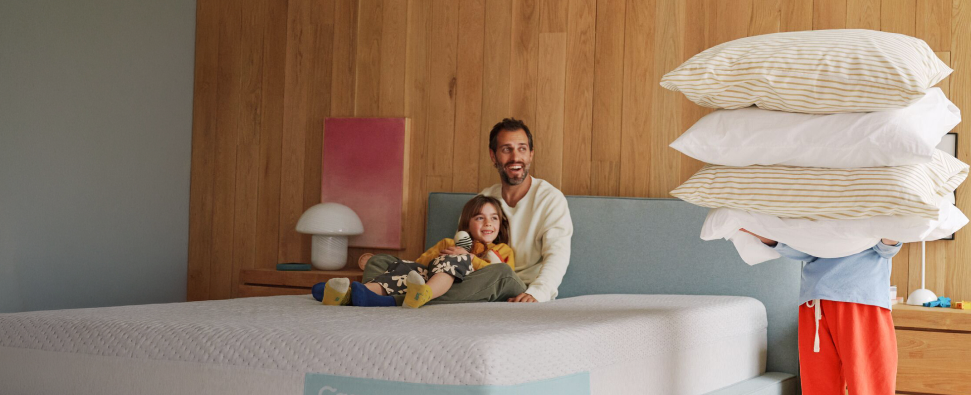 Man and child with a mattress and pillows in a bedroom setting