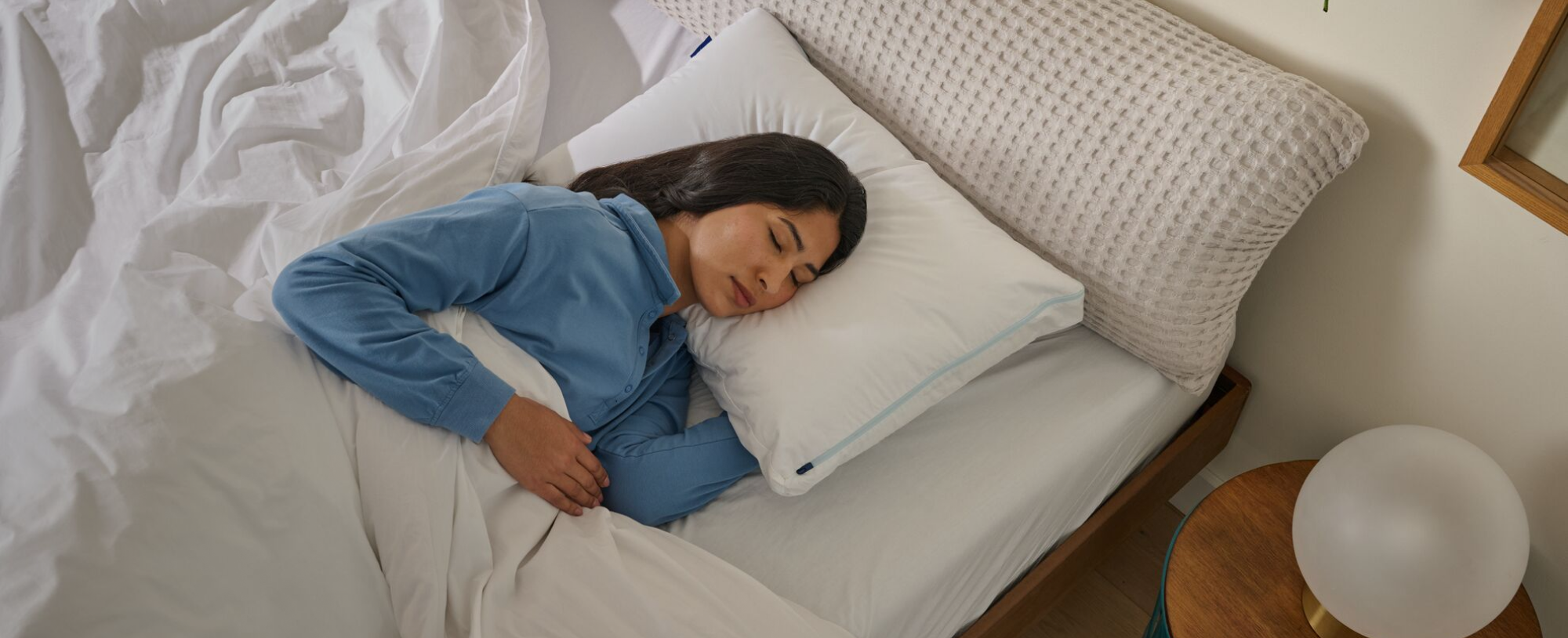 Woman sleeping on a bed with a white pillow and blue pajamas.