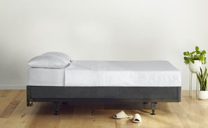 Side image of a bed against an empty wall. The bed is made with pillows and a sheet set. The mattress sits on top of Casper's Foundation, which is placed on a metal bed frame on a wooden floor.