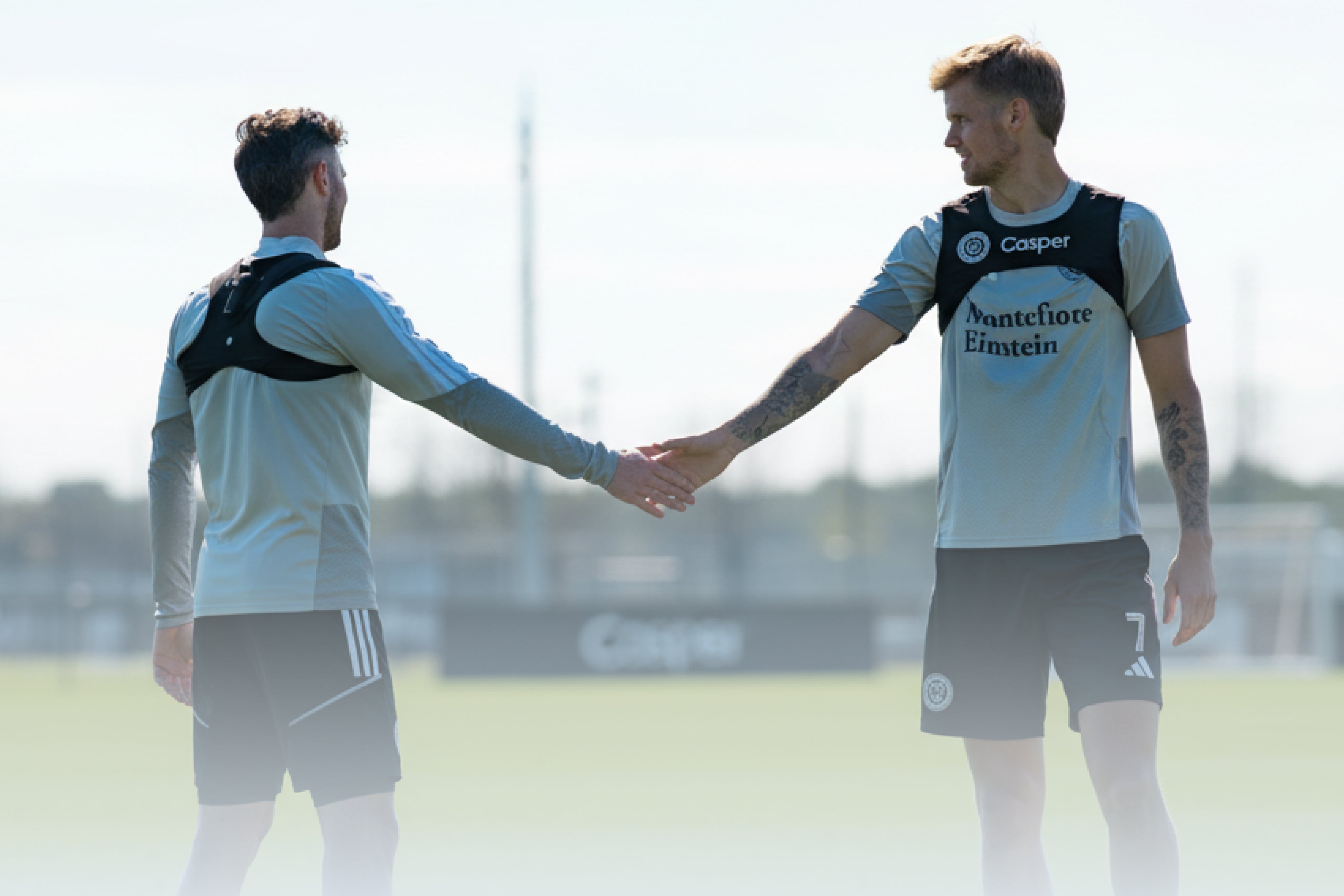 Two soccer players shaking hands on a field with 'Casper' branding.
