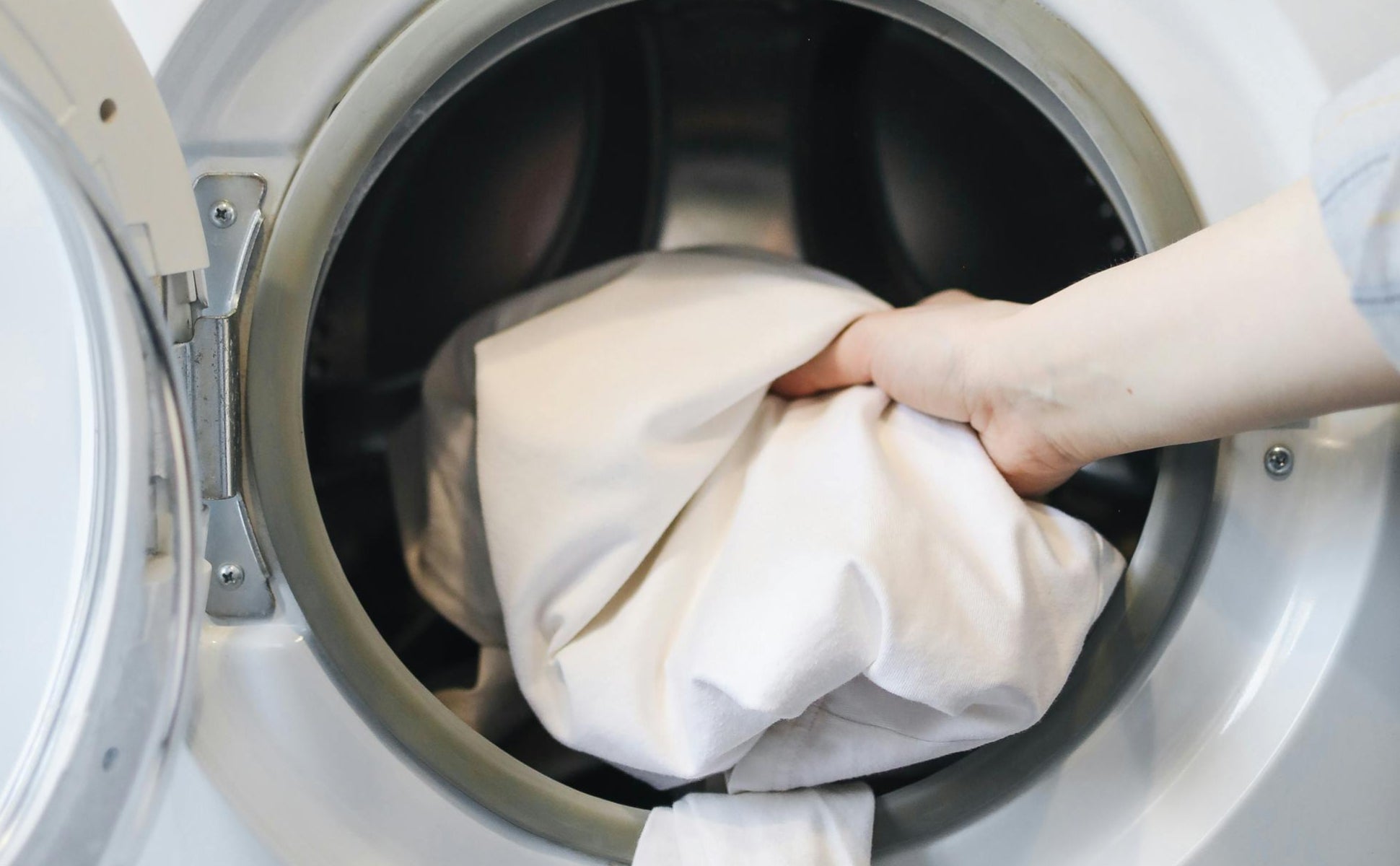 A person's hand placing the pillow into a washer, because the product is machine washable.