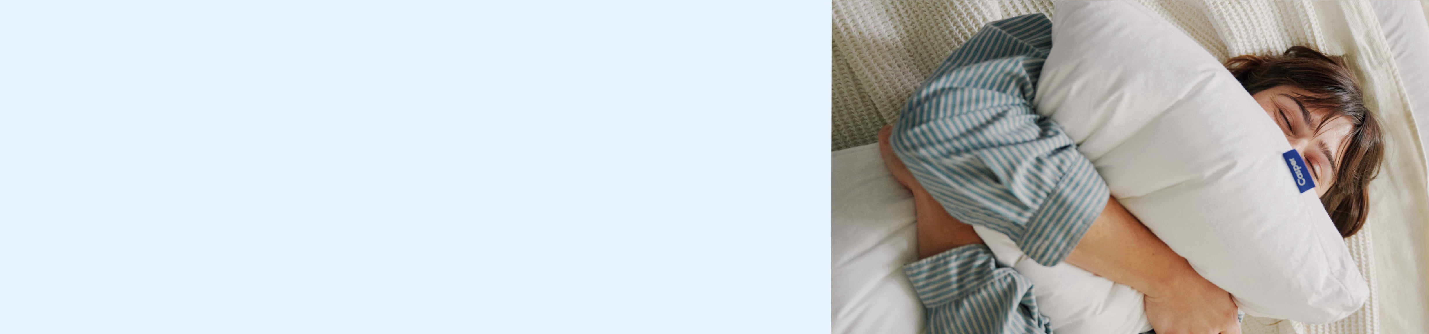 Light blue background. Image of a woman squeezing a pillow in bed.