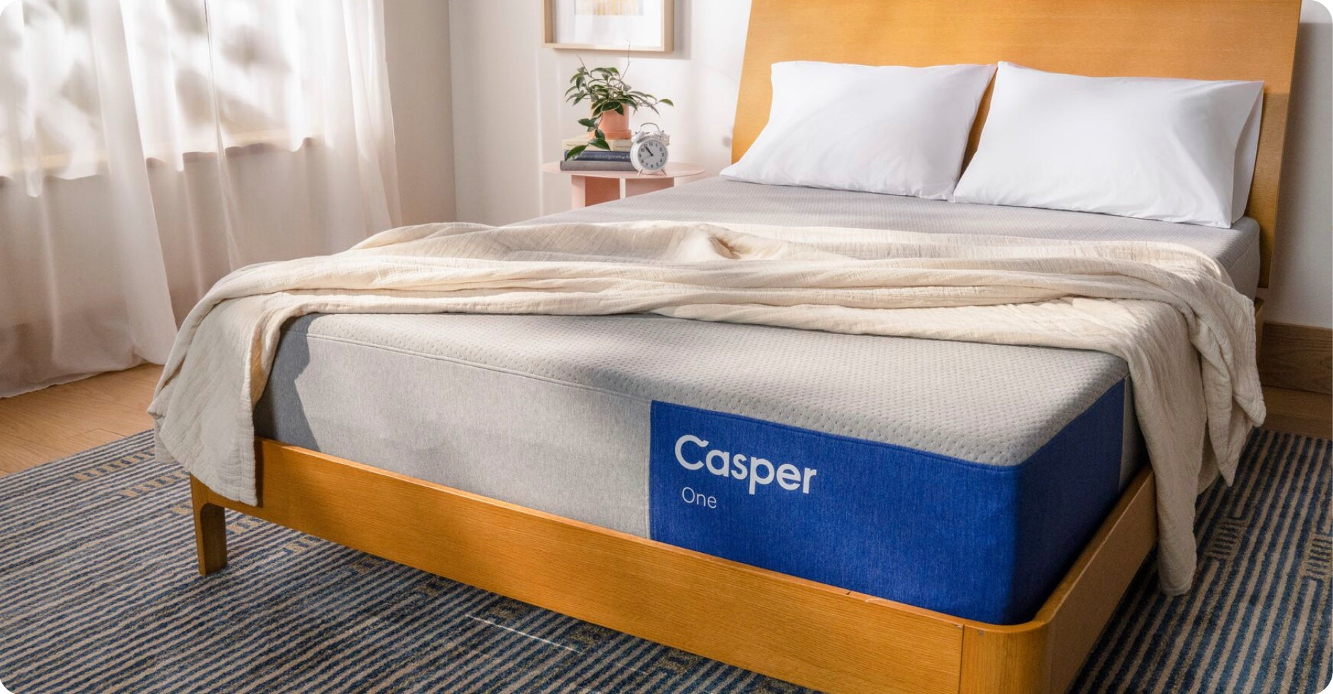 The One mattress on a bed frame with two pillows and a folded blanket on top.